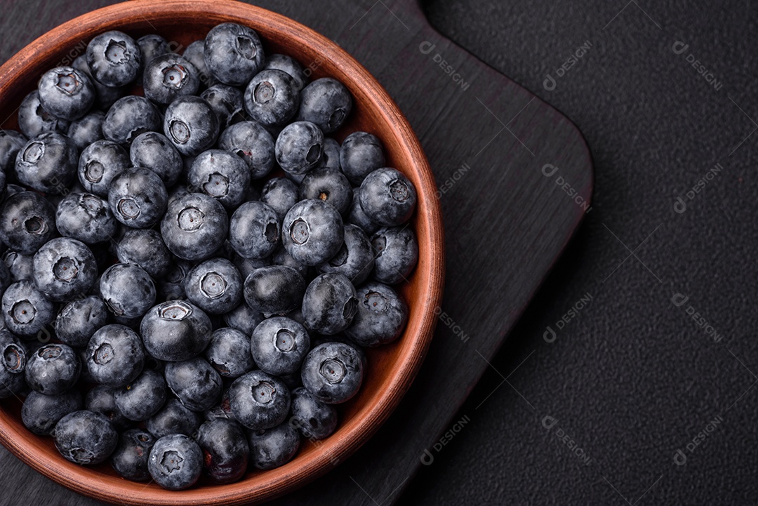 Deliciosos mirtilos doces frescos em uma tigela de cerâmica sobre um fundo escuro de concreto