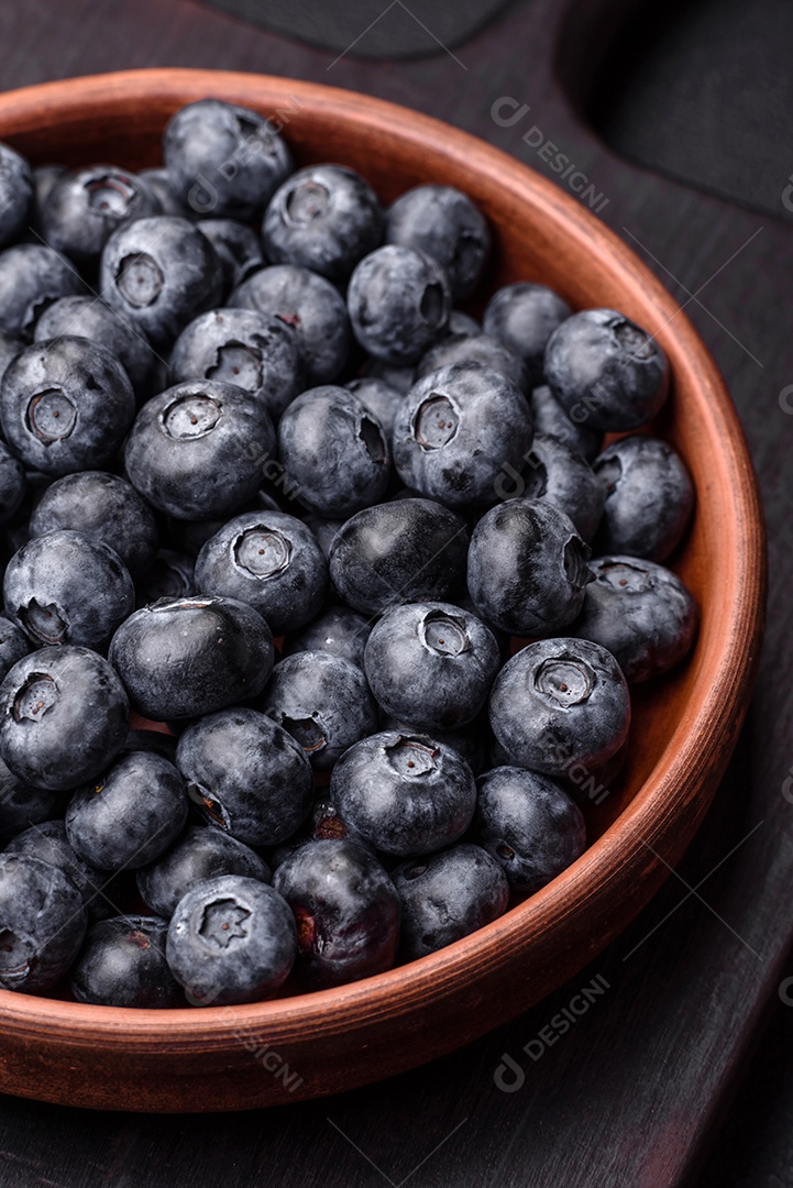 Deliciosos mirtilos doces frescos em uma tigela de cerâmica sobre um fundo escuro de concreto