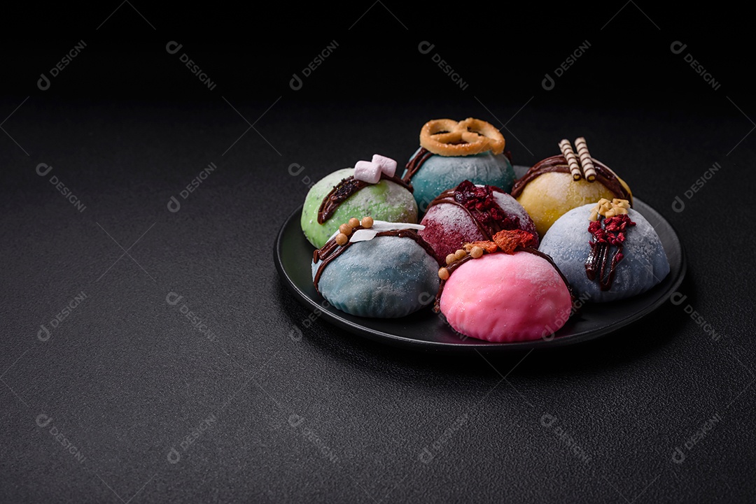 Deliciosas sobremesas mochi coloridas ou sorvete com massa de arroz e coberturas sobre um fundo escuro de concreto