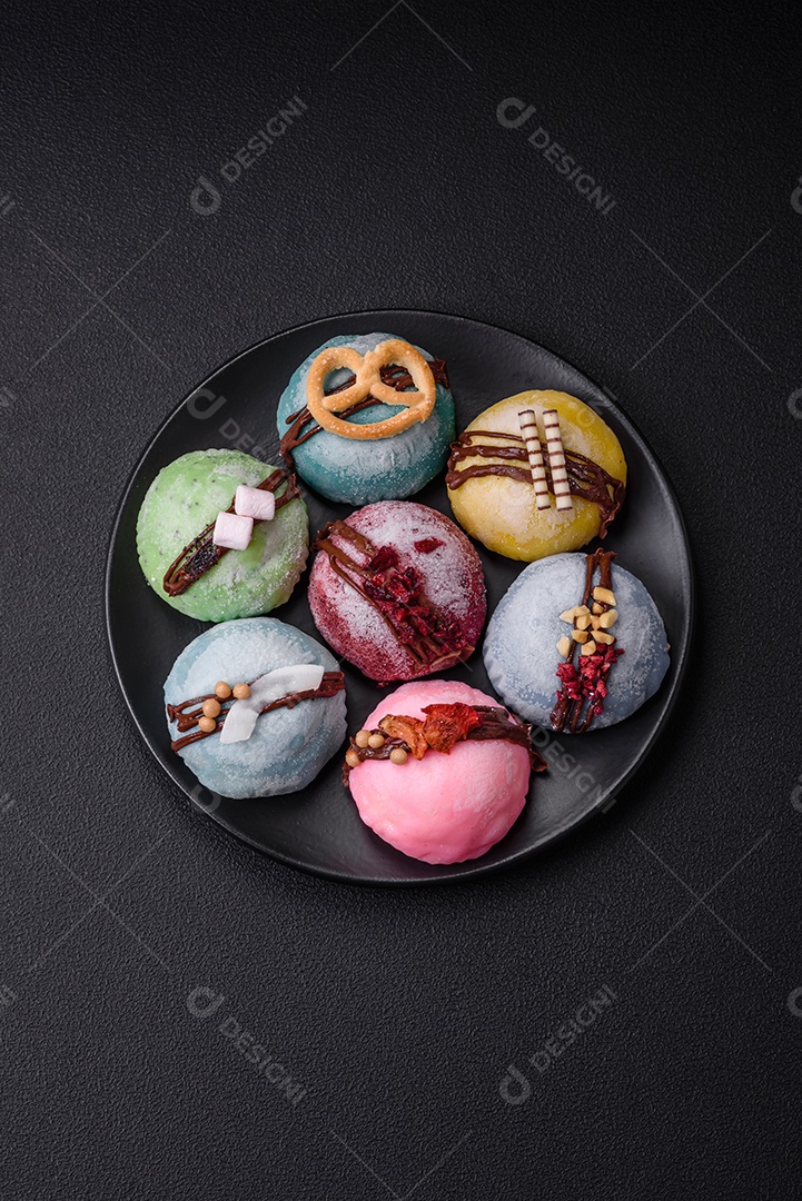 Deliciosas sobremesas mochi coloridas ou sorvete com massa de arroz e coberturas sobre um fundo escuro de concreto