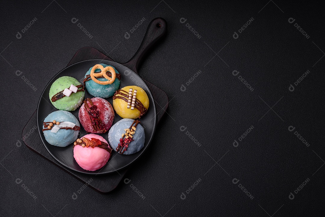 Deliciosas sobremesas mochi coloridas ou sorvete com massa de arroz e coberturas sobre um fundo escuro de concreto