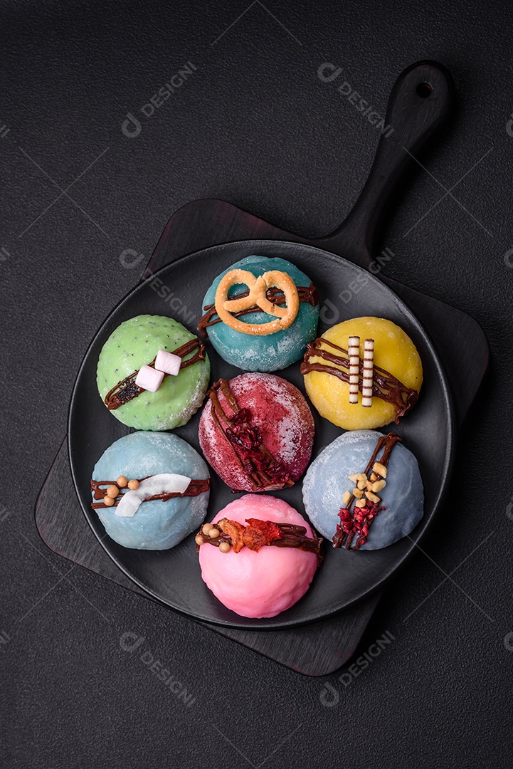 Deliciosas sobremesas mochi coloridas ou sorvete com massa de arroz e coberturas sobre um fundo escuro de concreto