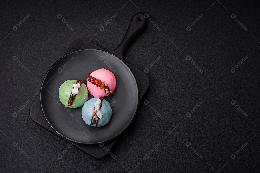 Deliciosas sobremesas mochi coloridas ou sorvete com massa de arroz e coberturas sobre um fundo escuro de concreto