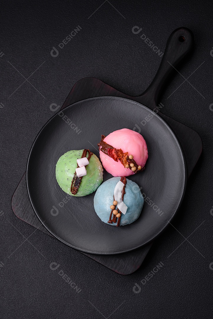 Deliciosas sobremesas mochi coloridas ou sorvete com massa de arroz e coberturas sobre um fundo escuro de concreto