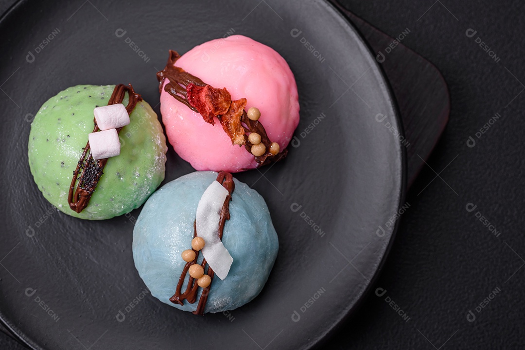 Deliciosas sobremesas mochi coloridas ou sorvete com massa de arroz e coberturas sobre um fundo escuro de concreto