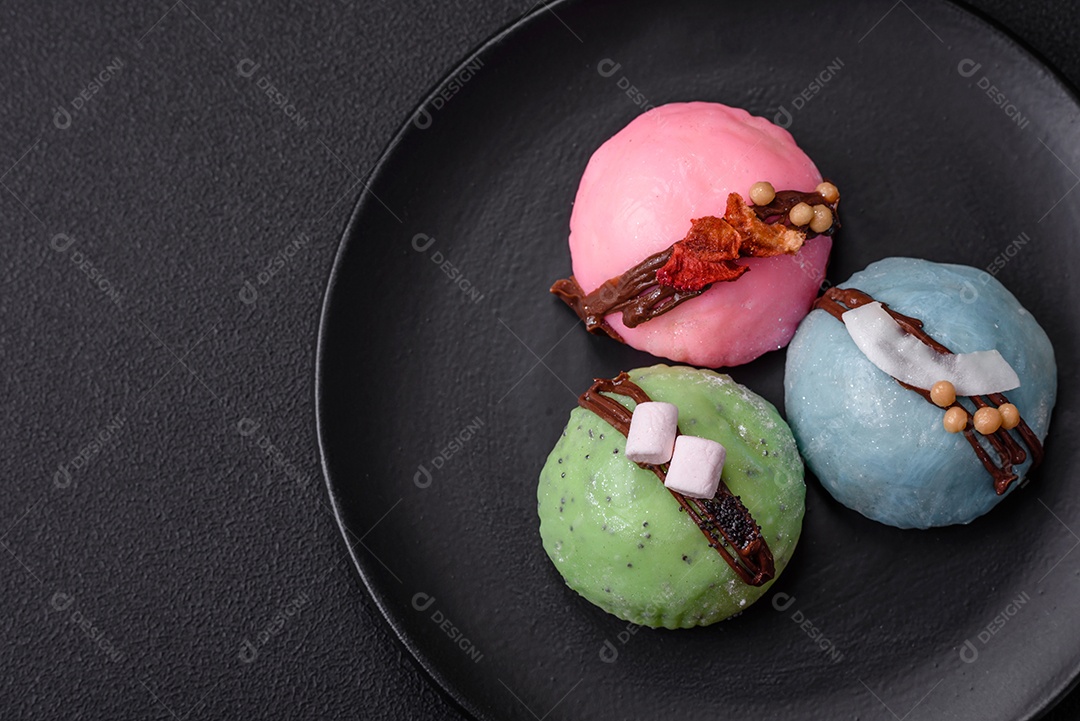 Deliciosas sobremesas mochi coloridas ou sorvete com massa de arroz e coberturas sobre um fundo escuro de concreto