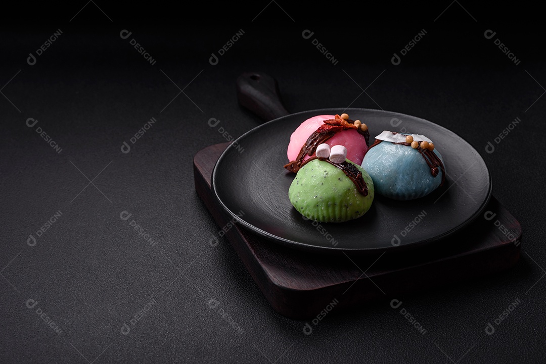 Deliciosas sobremesas mochi coloridas ou sorvete com massa de arroz e coberturas sobre um fundo escuro de concreto