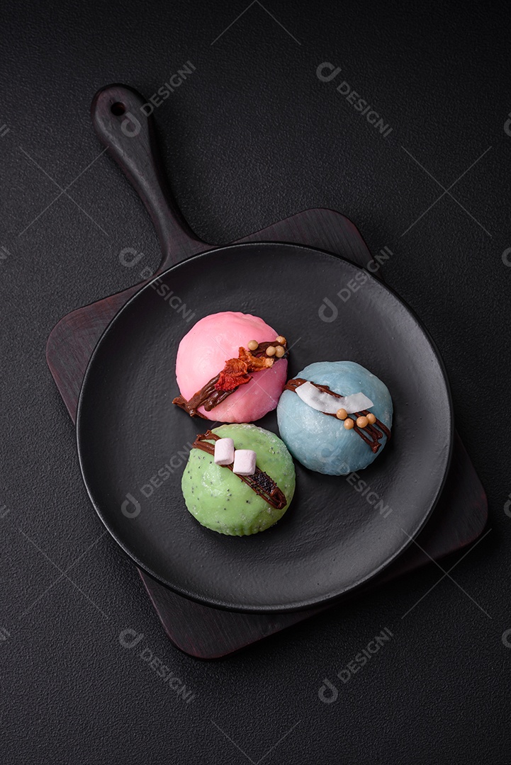 Deliciosas sobremesas mochi coloridas ou sorvete com massa de arroz e coberturas sobre um fundo escuro de concreto
