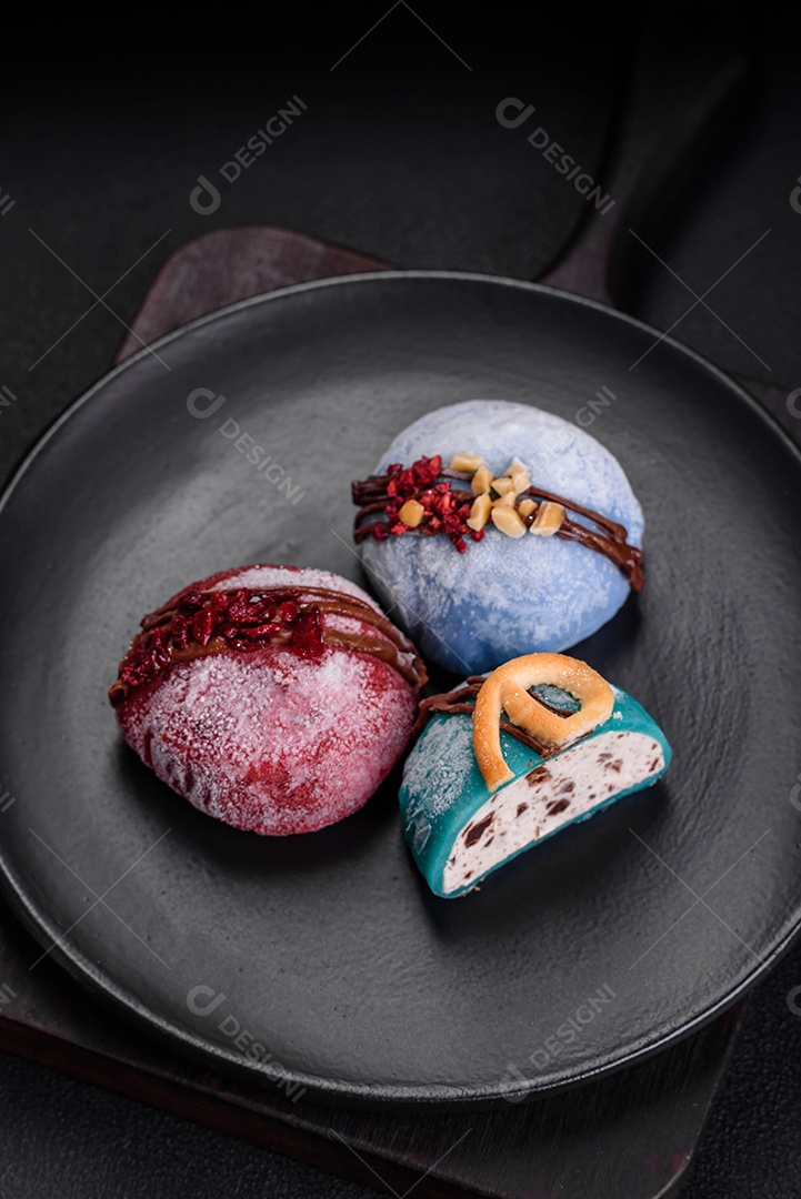 Deliciosas sobremesas mochi coloridas ou sorvete com massa de arroz e coberturas sobre um fundo escuro de concreto