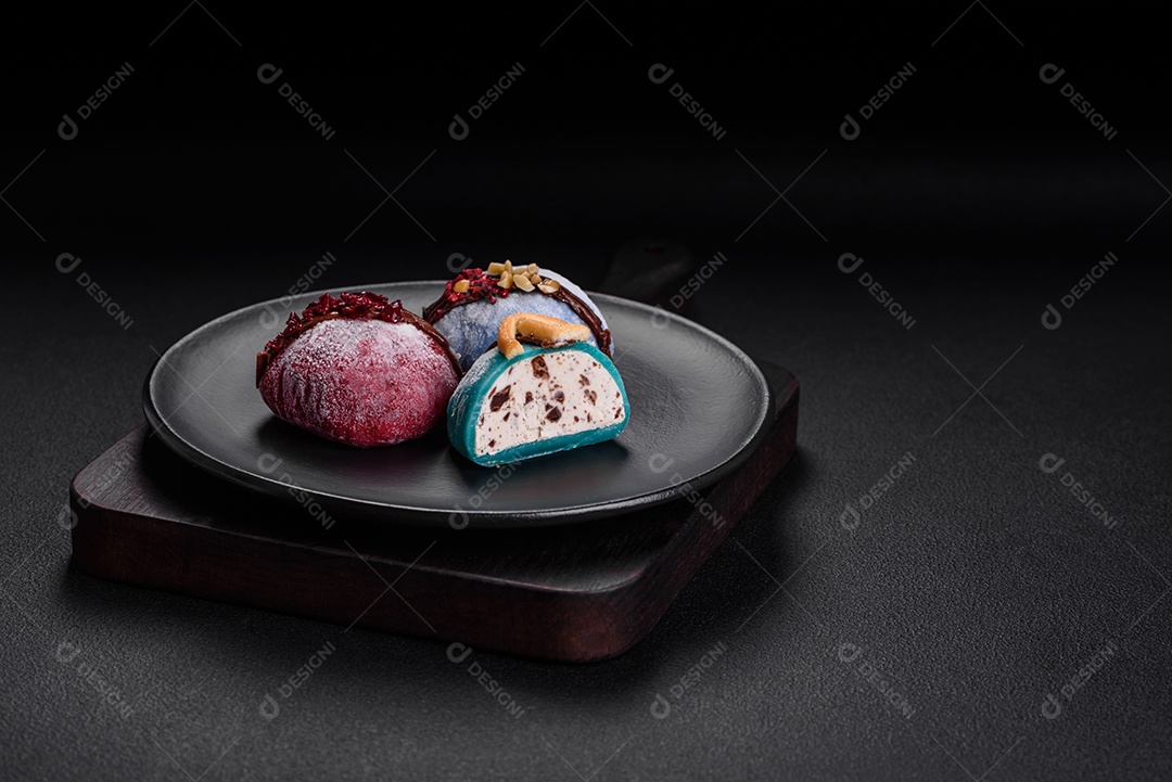 Deliciosas sobremesas mochi coloridas ou sorvete com massa de arroz e coberturas sobre um fundo escuro de concreto