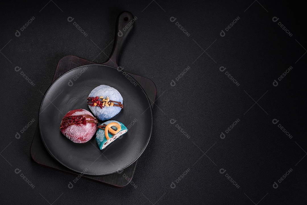 Deliciosas sobremesas mochi coloridas ou sorvete com massa de arroz e coberturas sobre um fundo escuro de concreto