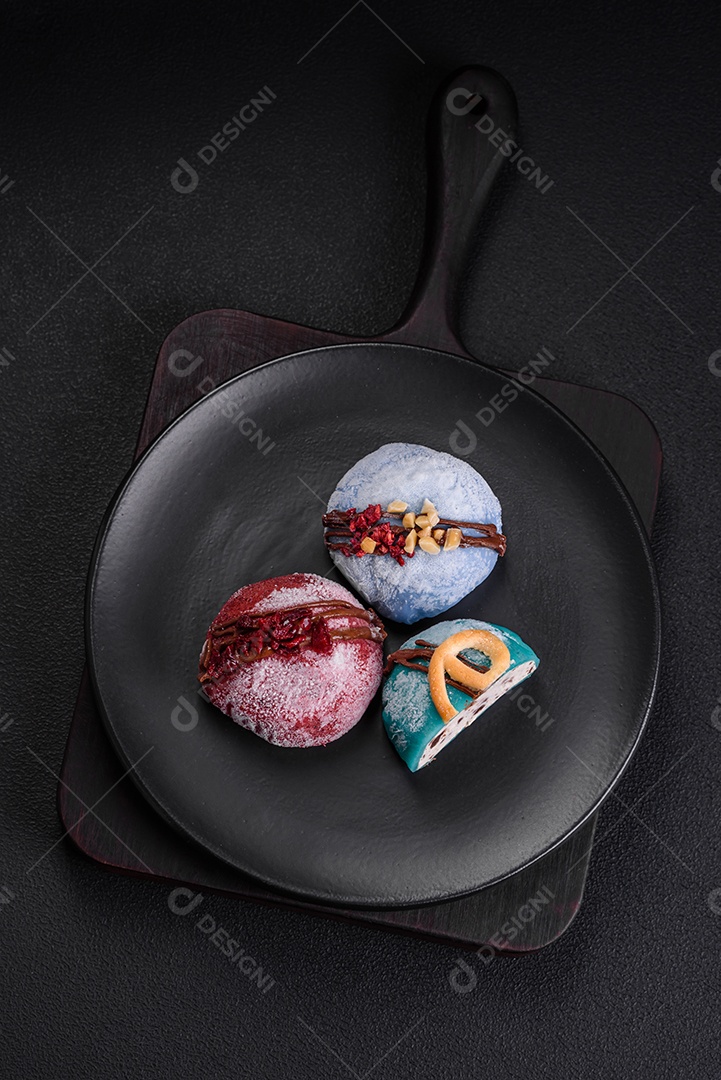 Deliciosas sobremesas mochi coloridas ou sorvete com massa de arroz e coberturas sobre um fundo escuro de concreto