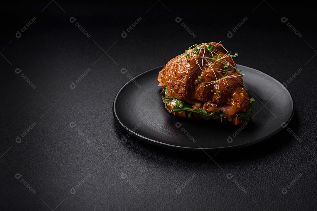 Delicioso croissant crocante com salmão, alface, queijo e tomate em um fundo escuro de concreto