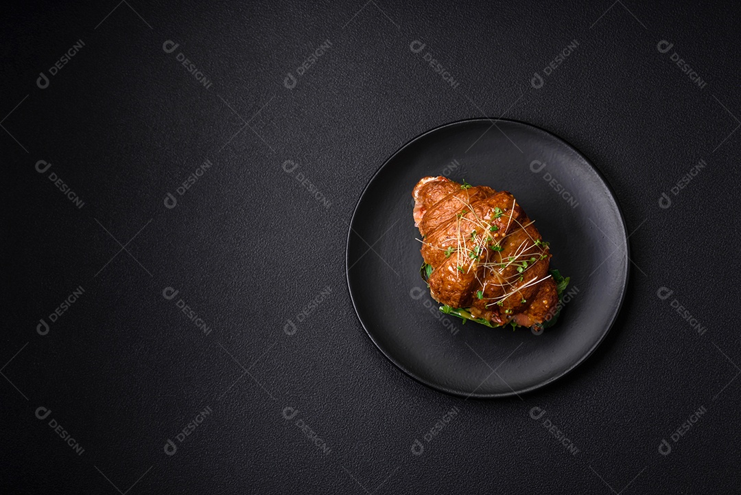 Delicioso croissant crocante com salmão, alface, queijo e tomate em um fundo escuro de concreto