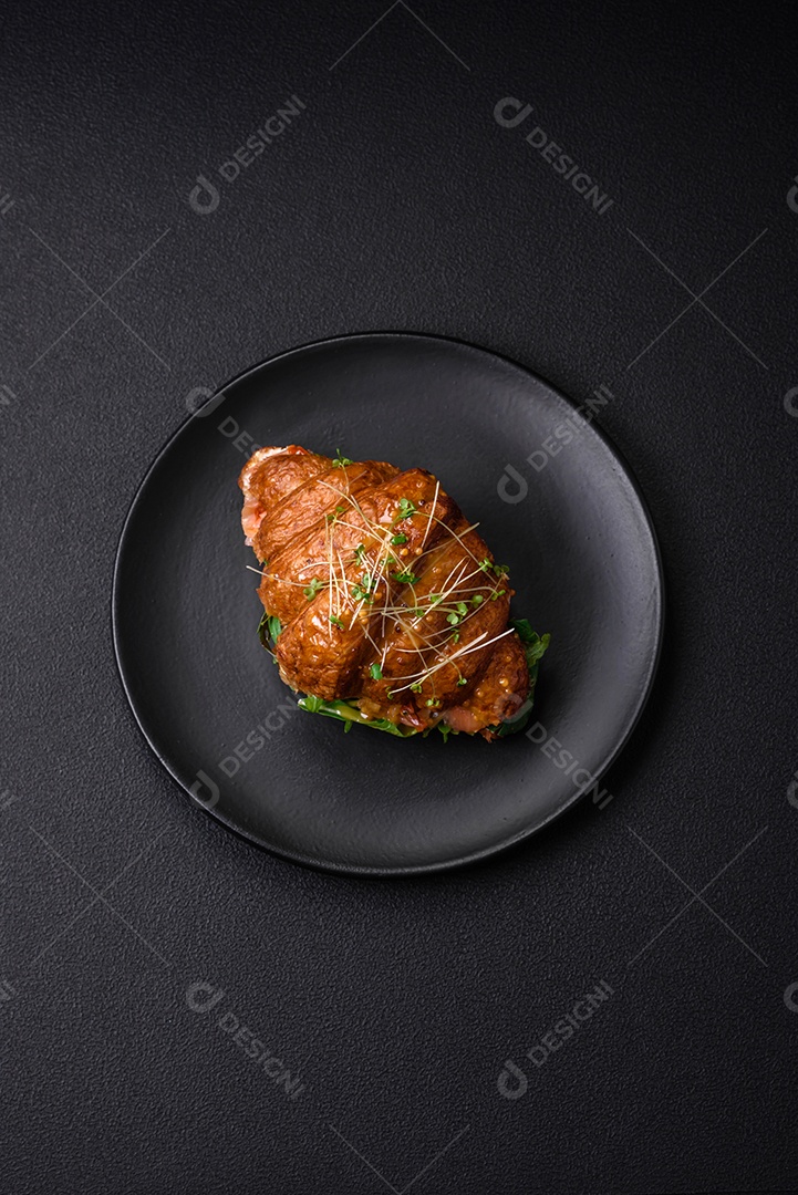 Delicioso croissant crocante com salmão, alface, queijo e tomate em um fundo escuro de concreto