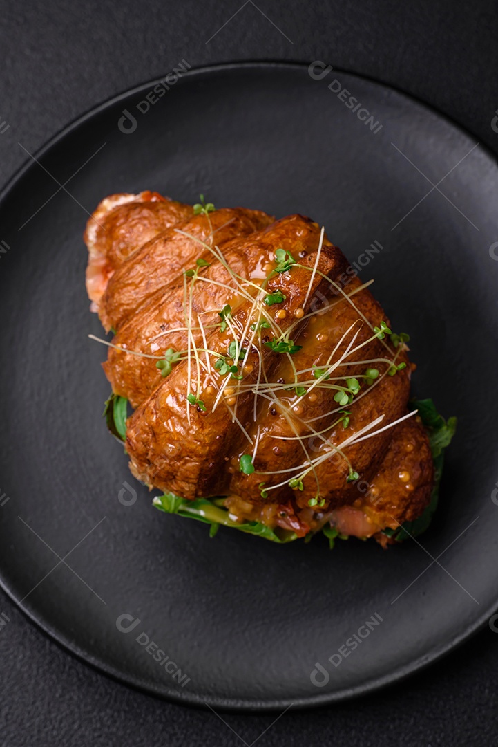 Delicioso croissant crocante com salmão, alface, queijo e tomate em um fundo escuro de concreto