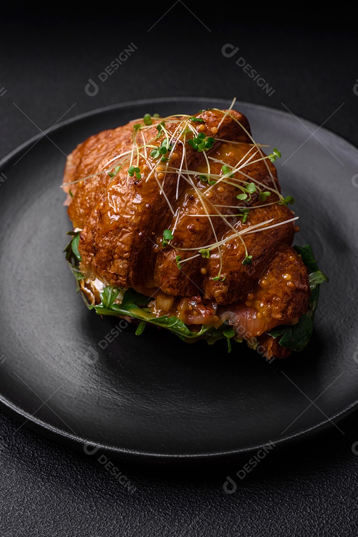 Delicioso croissant crocante com salmão, alface, queijo e tomate em um fundo escuro de concreto