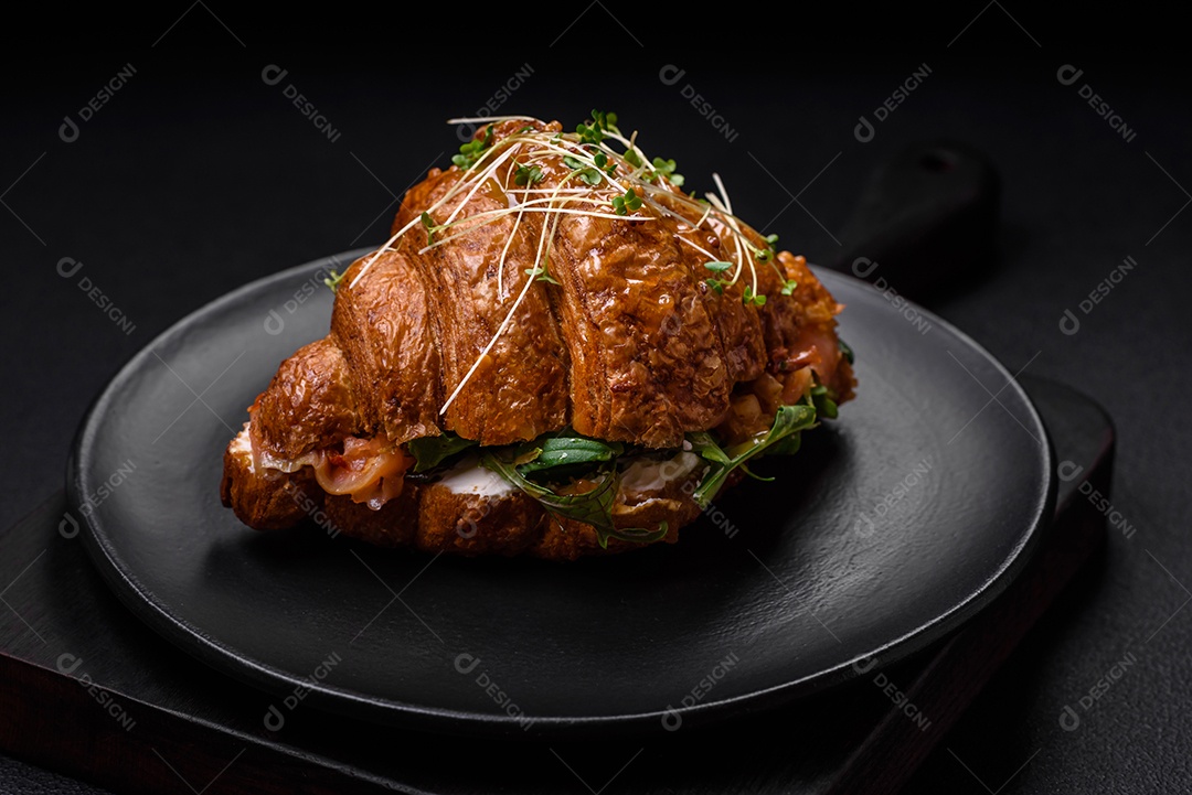 Delicioso croissant crocante com salmão, alface, queijo e tomate em um fundo escuro de concreto