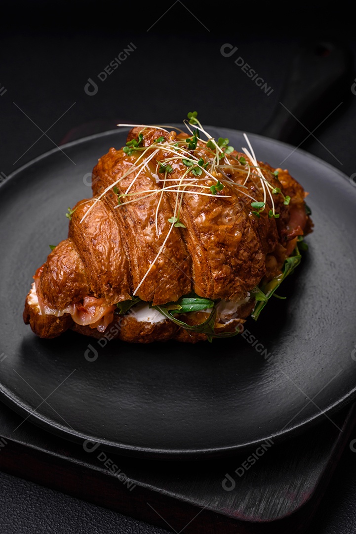 Delicioso croissant crocante com salmão, alface, queijo e tomate em um fundo escuro de concreto