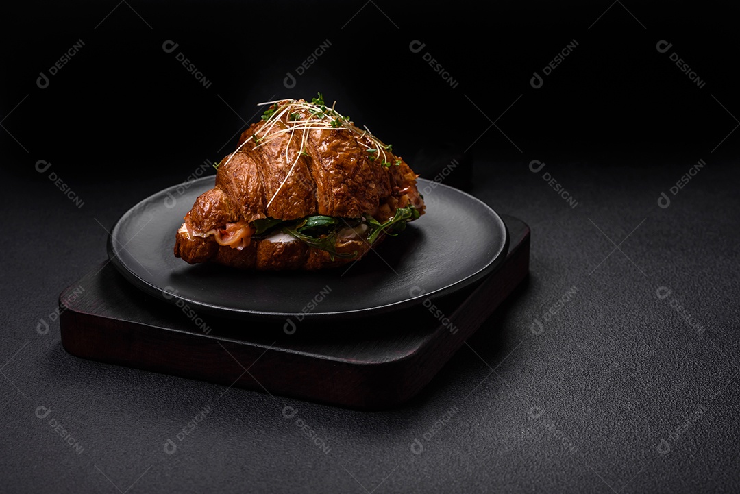 Delicioso croissant crocante com salmão, alface, queijo e tomate em um fundo escuro de concreto