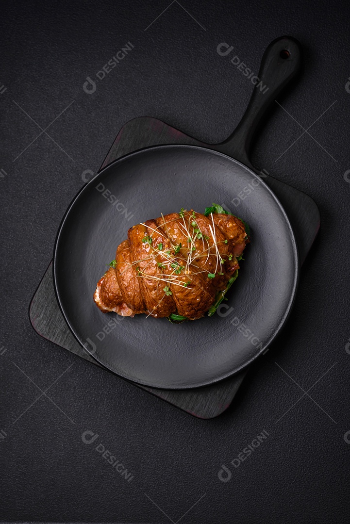 Delicioso croissant crocante com salmão, alface, queijo e tomate em um fundo escuro de concreto