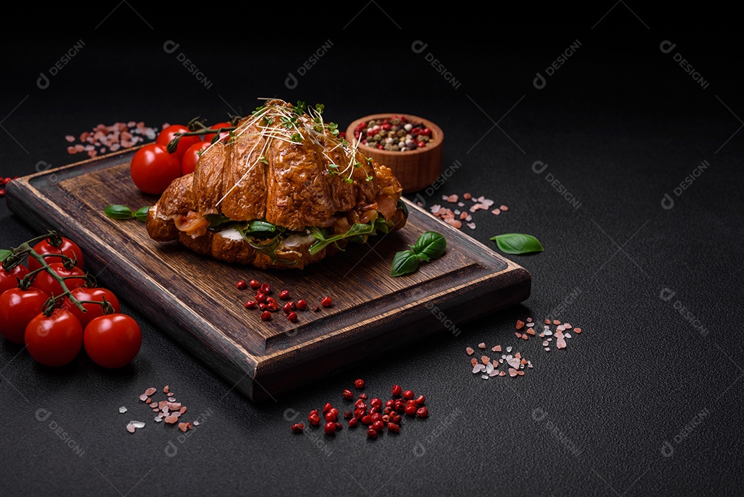 Delicioso croissant crocante com salmão, alface, queijo e tomate em um fundo escuro de concreto