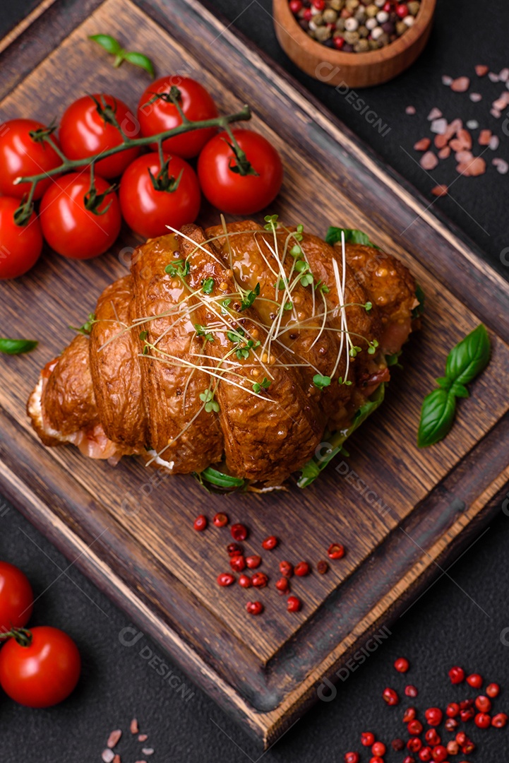 Delicioso croissant crocante com salmão, alface, queijo e tomate em um fundo escuro de concreto