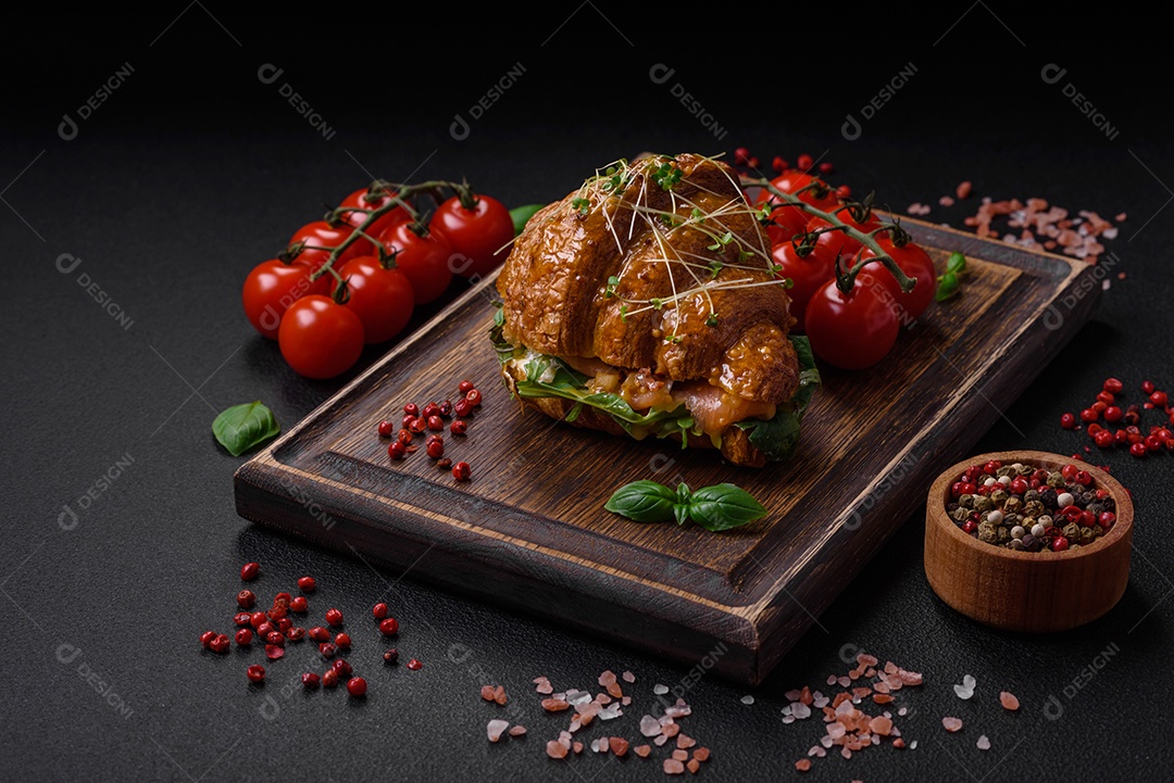 Delicioso croissant crocante com salmão, alface, queijo e tomate em um fundo escuro de concreto
