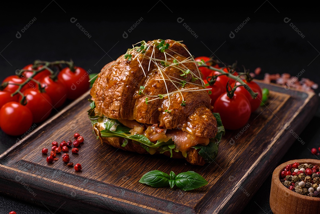 Delicioso croissant crocante com salmão, alface, queijo e tomate em um fundo escuro de concreto