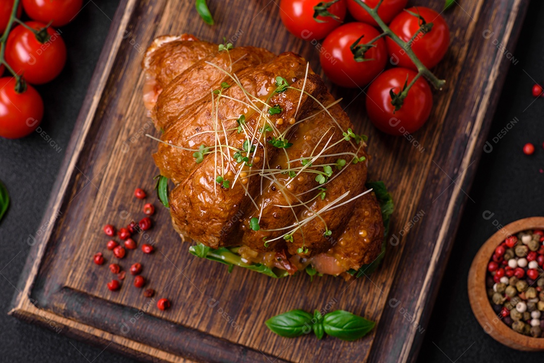 Delicioso croissant crocante com salmão, alface, queijo e tomate em um fundo escuro de concreto