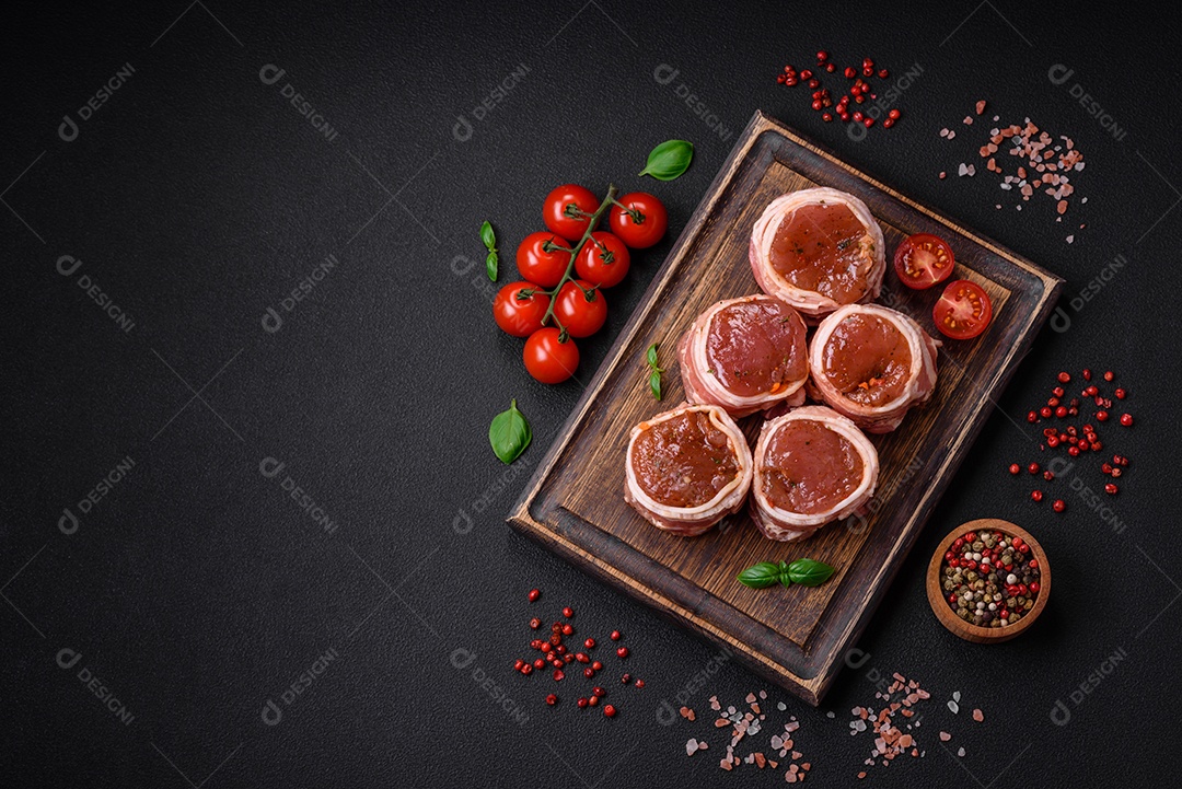 Deliciosos rolos de carne de porco ou frango crus e frescos embrulhados em bacon, com sal, especiarias e ervas sobre um fundo escuro de concreto