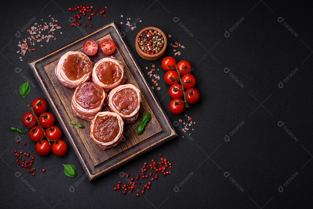 Deliciosos rolos de carne de porco ou frango crus e frescos embrulhados em bacon, com sal, especiarias e ervas sobre um fundo escuro de concreto