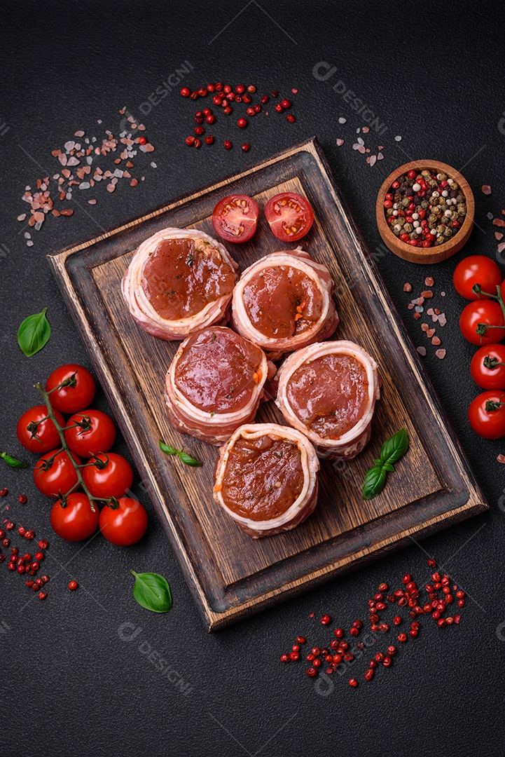 Deliciosos rolos de carne de porco ou frango crus e frescos embrulhados em bacon, com sal, especiarias e ervas sobre um fundo escuro de concreto