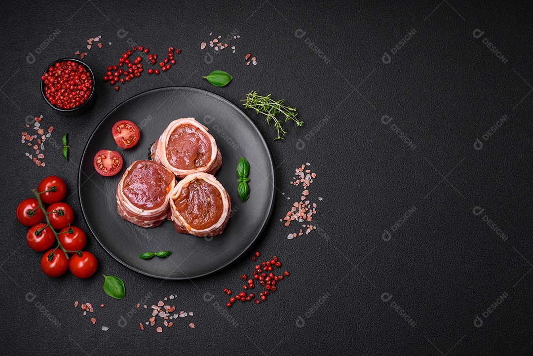 Deliciosos rolos de carne de porco ou frango crus e frescos embrulhados em bacon, com sal, especiarias e ervas sobre um fundo escuro de concreto