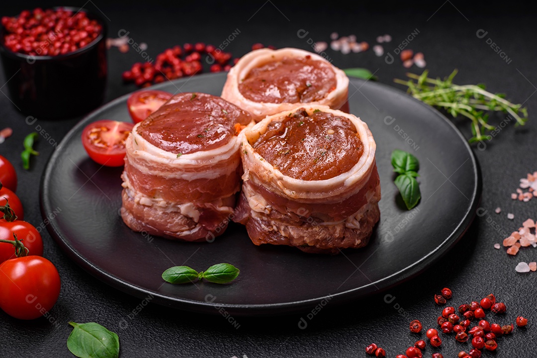 Deliciosos rolos de carne de porco ou frango crus e frescos embrulhados em bacon, com sal, especiarias e ervas sobre um fundo escuro de concreto