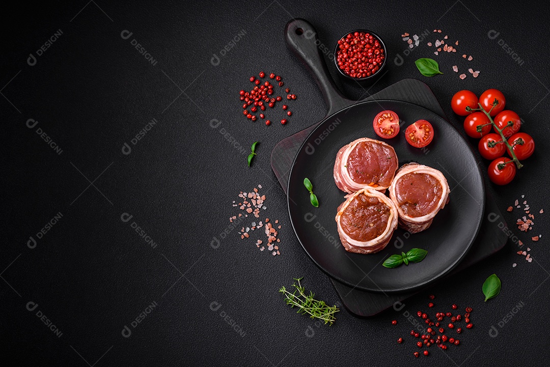 Deliciosos rolos de carne de porco ou frango crus e frescos embrulhados em bacon, com sal, especiarias e ervas sobre um fundo escuro de concreto