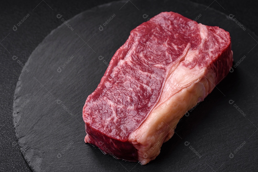 Bife de carne crua fresca com sal, especiarias e ervas sobre um fundo escuro de concreto