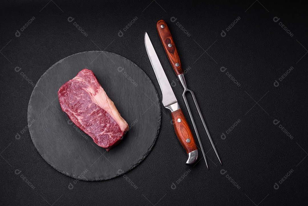 Bife de carne crua fresca com sal, especiarias e ervas sobre um fundo escuro de concreto