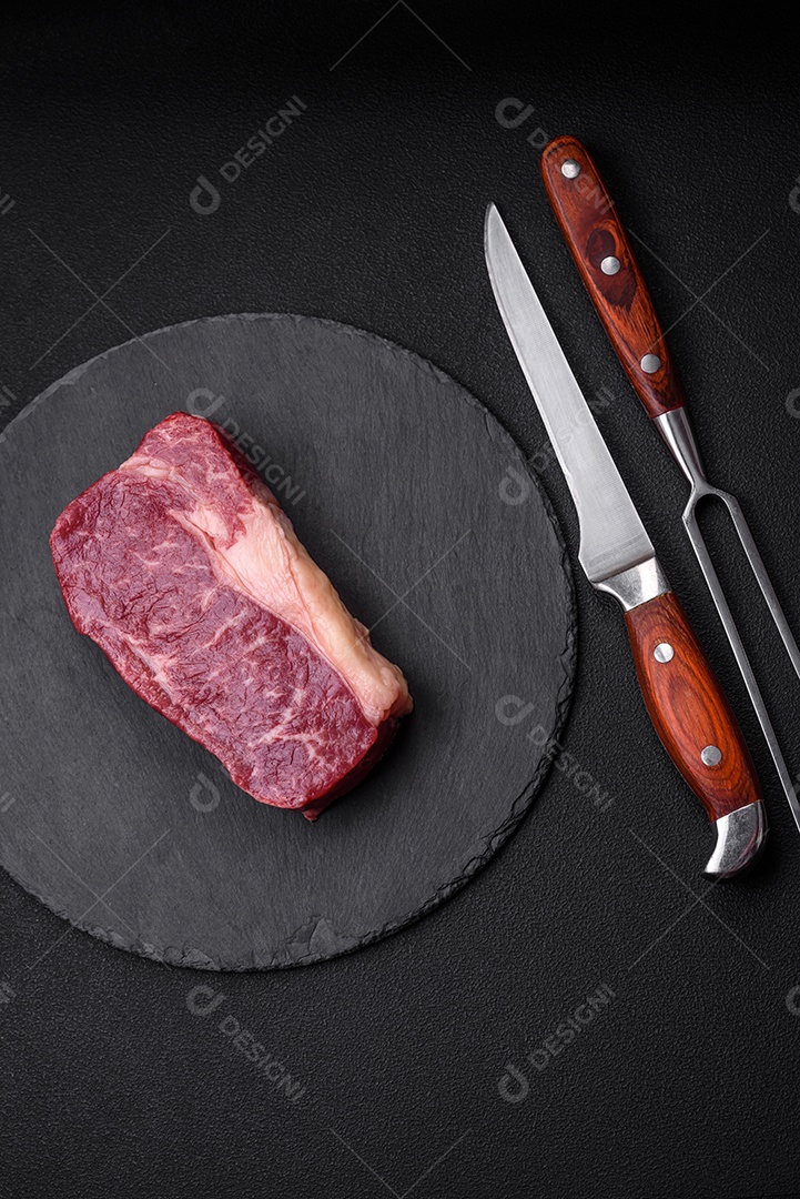 Bife de carne crua fresca com sal, especiarias e ervas sobre um fundo escuro de concreto