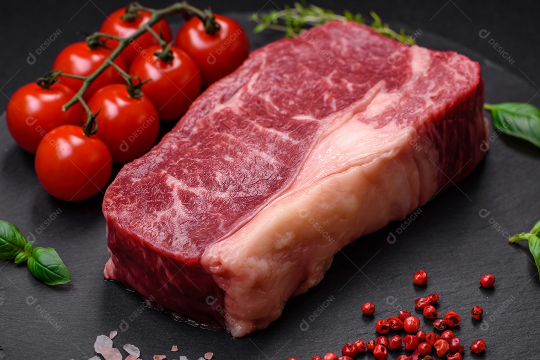 Bife de carne crua fresca com sal, especiarias e ervas sobre um fundo escuro de concreto