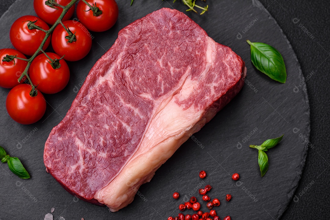 Bife de carne crua fresca com sal, especiarias e ervas sobre um fundo escuro de concreto