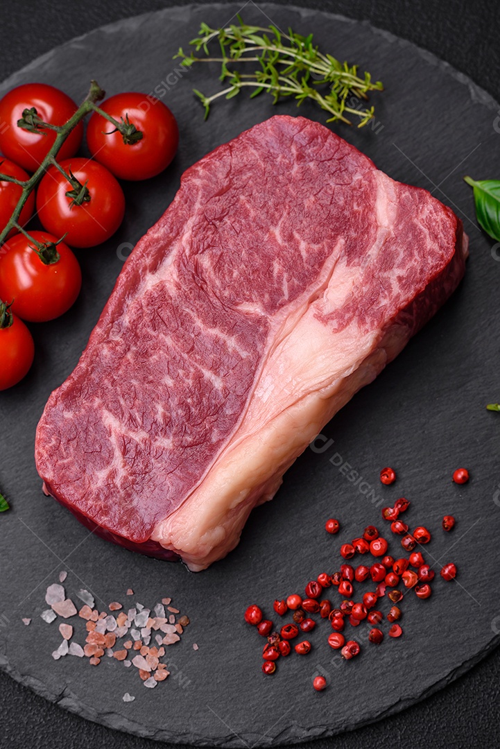 Bife de carne crua fresca com sal, especiarias e ervas sobre um fundo escuro de concreto