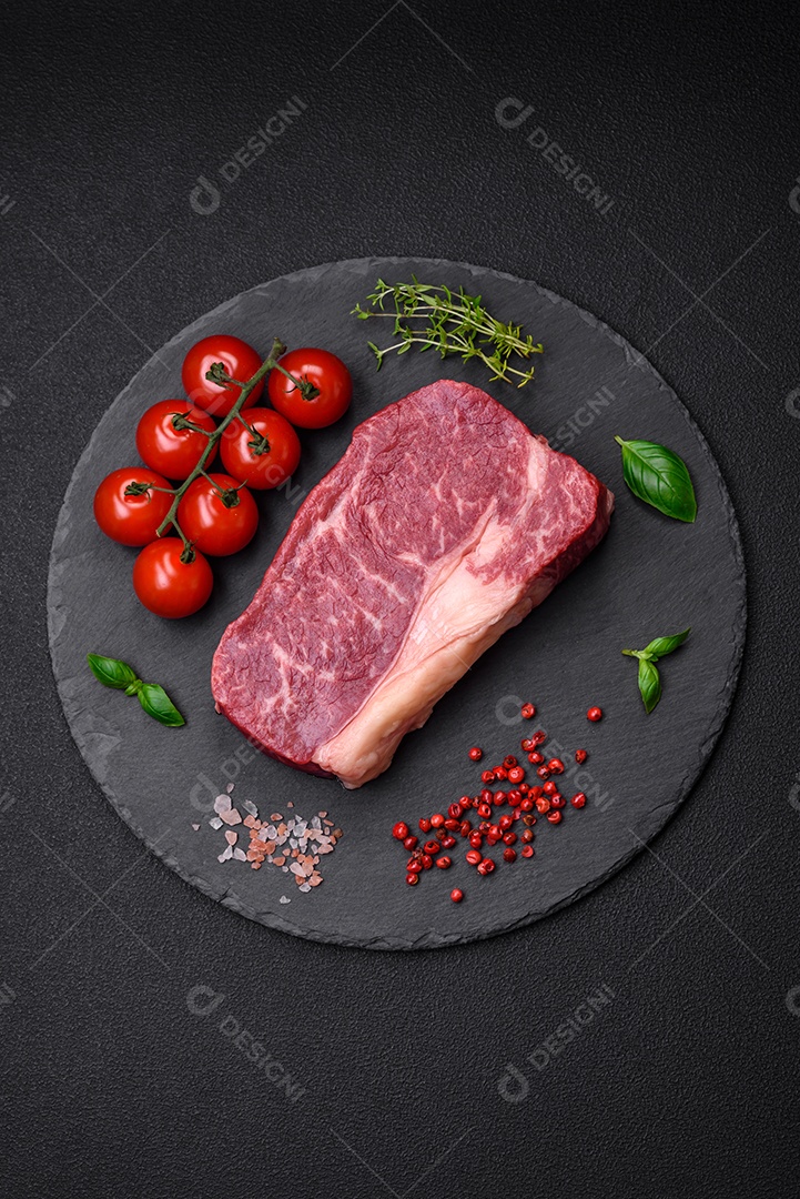 Bife de carne crua fresca com sal, especiarias e ervas sobre um fundo escuro de concreto