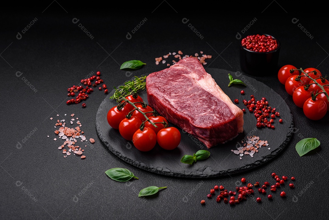 Bife de carne crua fresca com sal, especiarias e ervas sobre um fundo escuro de concreto