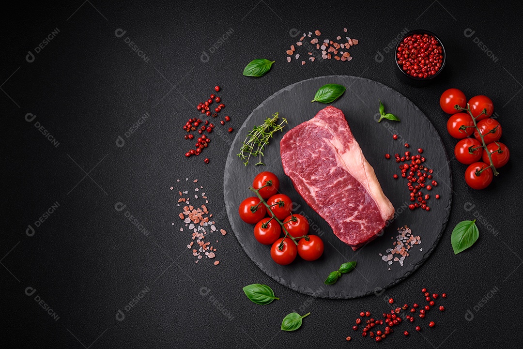 Bife de carne crua fresca com sal, especiarias e ervas sobre um fundo escuro de concreto