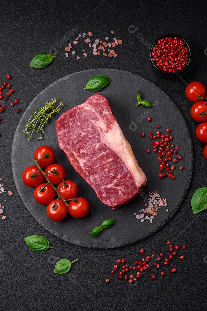 Bife de carne crua fresca com sal, especiarias e ervas sobre um fundo escuro de concreto