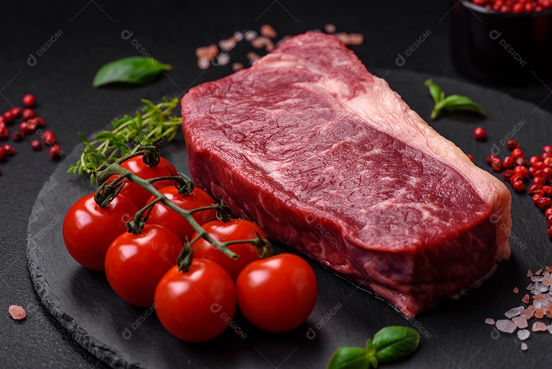 Bife de carne crua fresca com sal, especiarias e ervas sobre um fundo escuro de concreto