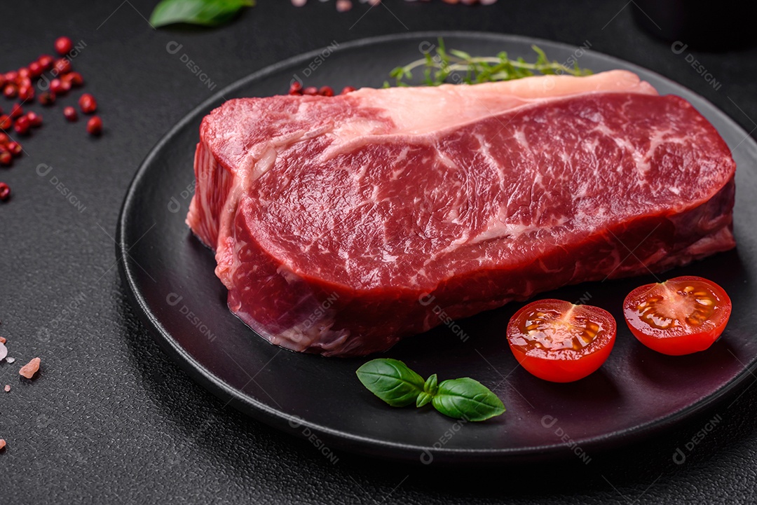 Bife de carne crua fresca com sal, especiarias e ervas sobre um fundo escuro de concreto