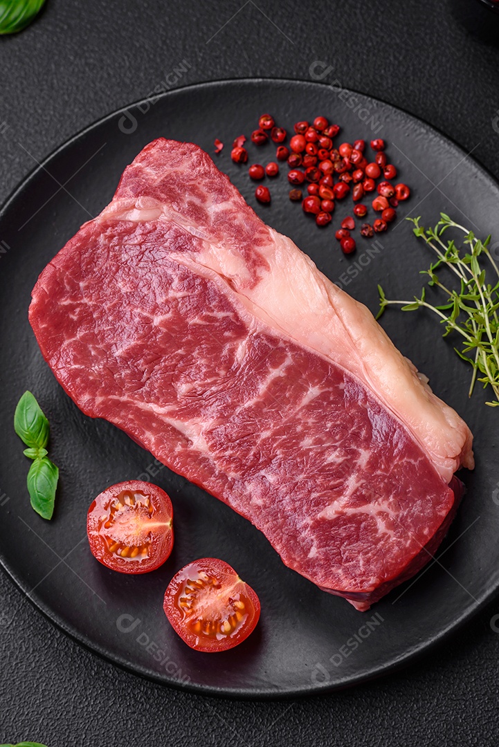 Bife de carne crua fresca com sal, especiarias e ervas sobre um fundo escuro de concreto