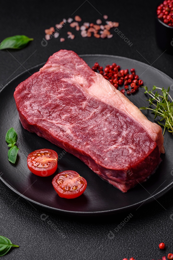 Bife de carne crua fresca com sal, especiarias e ervas sobre um fundo escuro de concreto